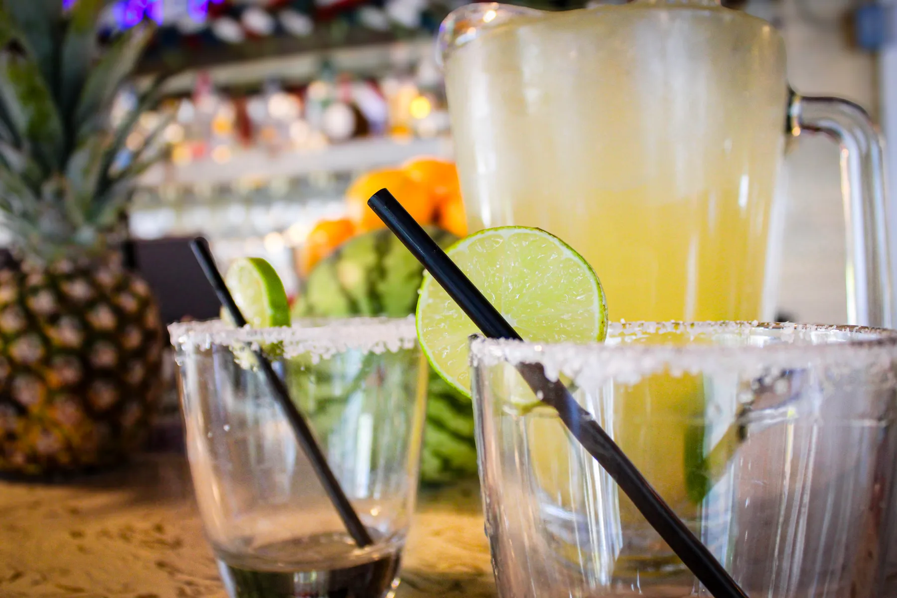 Two margaritas with salted rims and lime, a pitcher behind them