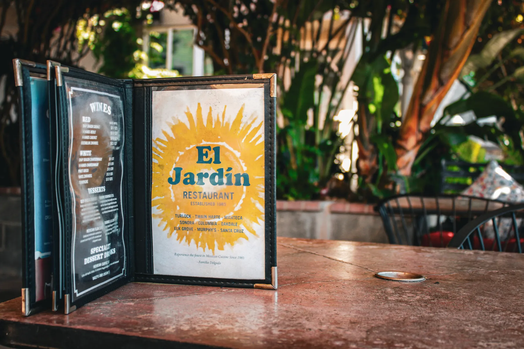 El Jardín's menu standing open on a patio table, sun logo and "Established 1985" on the cover