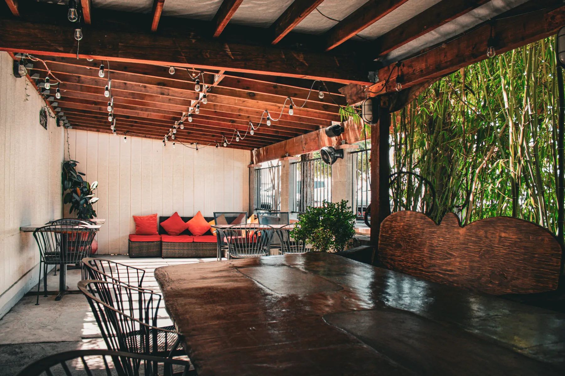 The covered patio: string lights over a long wood table, cushioned seating and bamboo along the far side